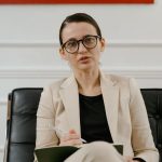 A woman in a blazer writing notes on a clipboard while sitting in an office.